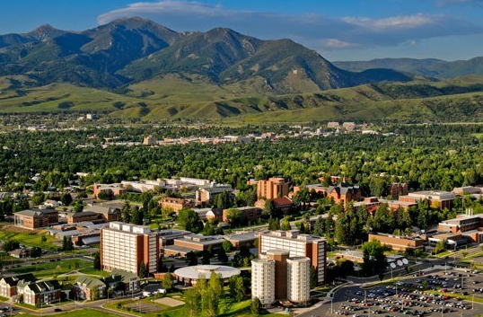 Bozeman, Montana overlook featuring the Bozeman welcome sign with downtown Bozeman, the Gallatin Valley, and surrounding neighborhoods beneath the Bridger Mountains.